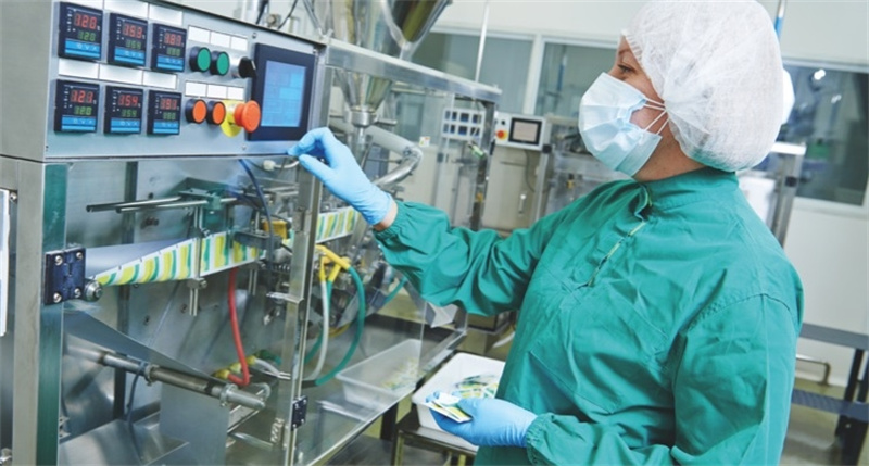 Pharmaceutical worker operating packaging machine in a cleanroom environment.